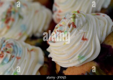 Chiudere la vista sulla piastra di crema bianca muffin con multi confettini colorati sulla parte superiore Foto Stock