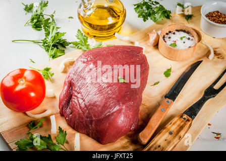 La cottura di filetto di manzo filetto. Grande tutto il pezzo di filetto di vitello sul tagliere con una forcella per la carne e le spezie (pepe, sale, prezzemolo, aglio, cipolle, Foto Stock