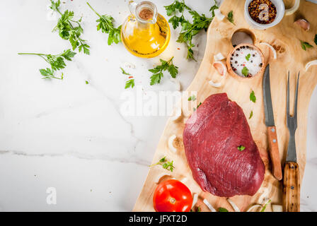 La cottura di filetto di manzo filetto. Grande tutto il pezzo di filetto di vitello sul tagliere con una forcella per la carne e le spezie (pepe, sale, prezzemolo, aglio, cipolle, Foto Stock