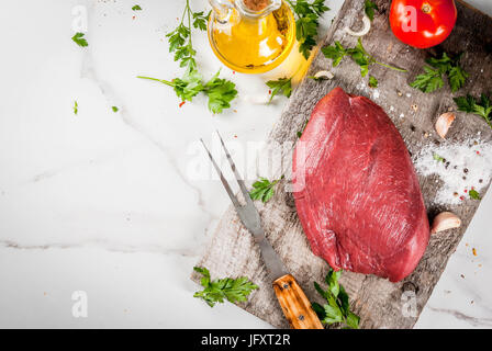 La cottura di filetto di manzo filetto. Grande tutto il pezzo di filetto di vitello su una vecchia scheda di taglio con una forcella per la carne e le spezie (pepe, sale, prezzemolo, aglio, Foto Stock