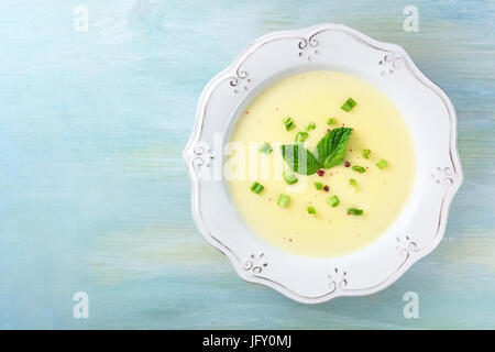 Una foto aerea di vichyssoise, un francese di patate e porri minestra con cipollotti tritati, grani di pepe rosa e le foglie di menta per la decorazione su un te Foto Stock