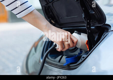 Mano in una maglia a strisce tenendo un caricabatterie per l'e-car Foto Stock