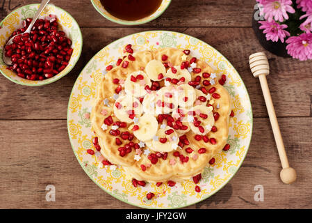 Morbido cuore belga cialde sagomate con banana e melograno, decorazione di zucchero stelle, ricoperte di miele. In legno rustico sfondo, vista dall'alto, vicino-u Foto Stock