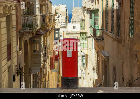 Una fotografia di un vecchio British postbox in piedi di La Valletta, Malta. I vecchi edifici in pietra di La Valletta circondano l'objet e il Mediterraneo Foto Stock