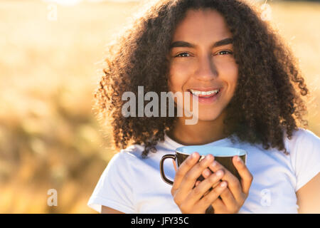 Bella felice razza mista americano africano ragazza adolescente femmine giovane donna sorridente con denti perfetto bianco,di bere il caffè o il tè all'aperto Foto Stock