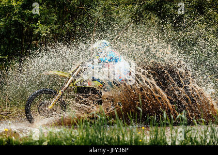 Motociclista attraversa la pozzanghera schizzi di acqua e sporcizia Foto Stock