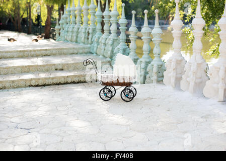 La bambola della PRAM. Bambola Vintage passeggino messo su per le scale di un bellissimo lago. Carrello retrò bambole fatte di rattan e pizzo bianco. Foto Stock