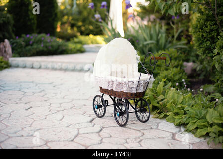 La bambola della PRAM. Bambola Vintage passeggino posto sulla passerella di pietra, vicolo in un bellissimo giardino con fiori ed alberi intorno. Carrello retrò bambole fatte di ra Foto Stock