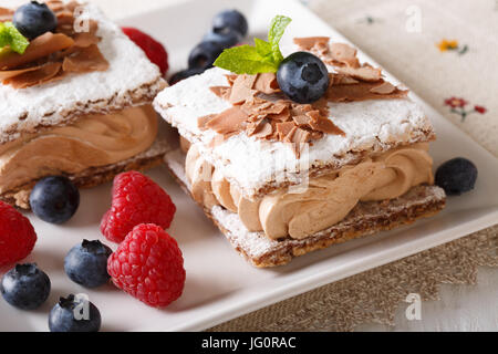 Bellissimo il dessert: torta al cioccolato con crema di caffè, lamponi e mirtilli close-up su una piastra orizzontale. Foto Stock