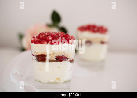 In casa layered dessert con mascarpone, il cioccolato con la panna, fragole fresche, cookie, melograno. Il formaggio in un bicchiere. Sfondo bianco, alta chiave, s Foto Stock