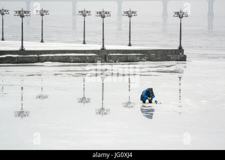 Il pescatore è la pesca sul ghiaccio di un fiume congelato in un inizio di mattinata nebbiosa. Dnepropetrovsk, Ucraina Foto Stock