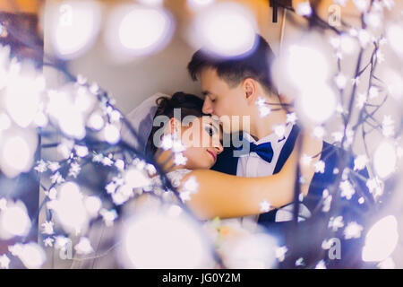 Lato romantico ritratto di coppie di sposi novelli dietro la luce ghirlande. Foto Stock
