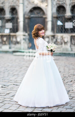 A tutta lunghezza indietro foto della sposa nel lungo abito da sposa con il bouquet. Posizione strada. Foto Stock