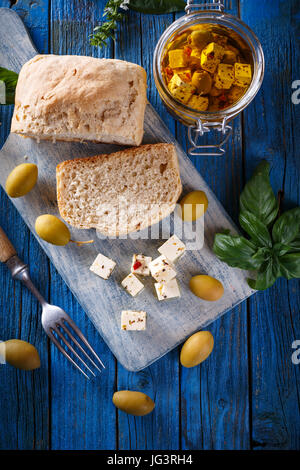 Tagliate a cubetti il formaggio feta con olive su blu sullo sfondo di legno Foto Stock