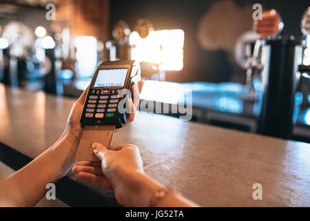 Le mani della donna pagando bill utilizzando una carta di credito presso il bar. Ritagliato shot della femmina alla fabbrica di birra facendo il pagamento senza contanti. Foto Stock