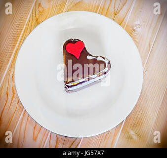 Forma di cuore torta al cioccolato con sugare cuore rosso sulla piastra bianca, close up, isolata. Foto Stock