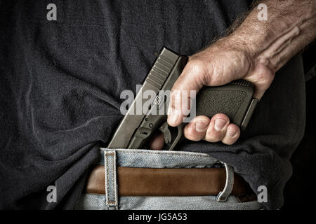 Un uomo con una pistola nella sua cintura e afferra la maniglia in preparazione per tirare l'arma Foto Stock