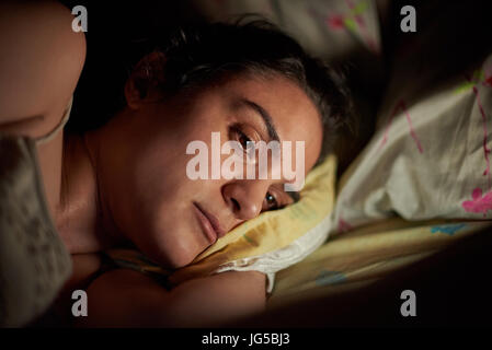 Ritratto di giovane donna utilizzando tablet a letto. Lettura della ragazza dalla tavoletta digitale di notte Foto Stock