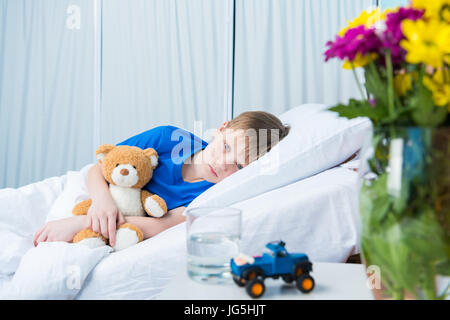 Malati little boy abbracciando Teddy bear e giacente in letto di ospedale Foto Stock