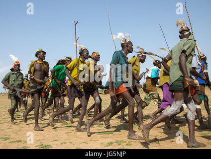 Gli uomini in esecuzione in linea con le armi durante la fiera ox cerimonia nella tribù Dassanech, Turkana County, Omorate, Etiopia Foto Stock