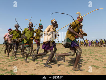 Gli uomini in esecuzione in linea con le armi durante la fiera ox cerimonia nella tribù Dassanech, Turkana County, Omorate, Etiopia Foto Stock