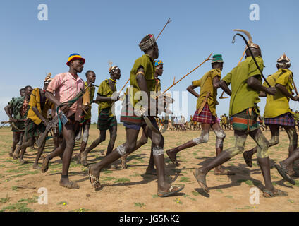 Gli uomini in esecuzione in linea con le armi durante la fiera ox cerimonia nella tribù Dassanech, Turkana County, Omorate, Etiopia Foto Stock