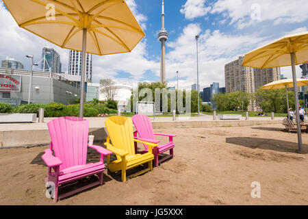 Toronto, Canada - 26 Giugno 2017: Tre vuoto colorate sedie a sdraio sulla spiaggia di Toronto con la CN Tower a distanza Foto Stock