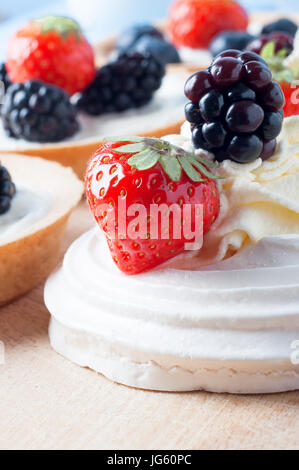 In prossimità di una meringa con volute di panna fresca e bacche (fragola e blackberry) su un tagliere di legno. In messa a fuoco morbida di lato Foto Stock