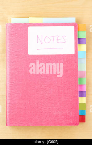 Notebook rosa su un legno chiaro dello sfondo. White " Note " etichetta sul coperchio, tre divisori a linguetta di sezionamento libro lungo il bordo superiore e quindici lungo diritto sid Foto Stock