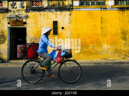 Una donna vietnamita vanno in bicicletta in una strada a Hoi An, Vietnam Foto Stock