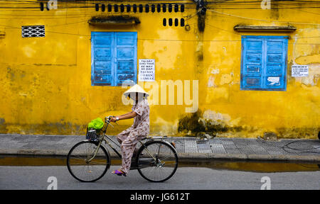 Una donna vietnamita vanno in bicicletta in una strada a Hoi An, Vietnam Foto Stock