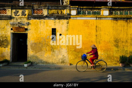 Una donna vietnamita vanno in bicicletta in una strada a Hoi An, Vietnam Foto Stock