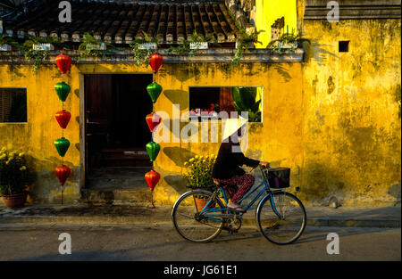 Una donna vietnamita vanno in bicicletta in una strada a Hoi An, Vietnam Foto Stock