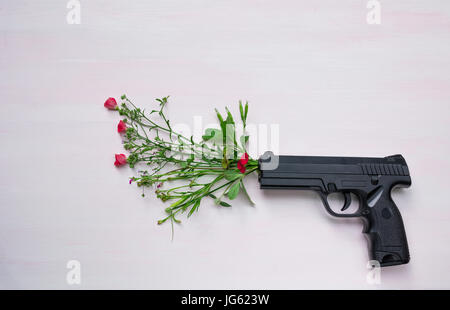 Pistola su sfondo di legno con fiori.La guerra e la pace piena con la mano la pistola. Foto Stock