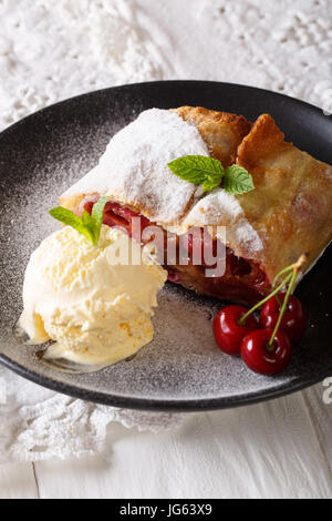 Pane appena sfornato dolci strudel di ciliegie con gelato alla vaniglia close-up su una piastra. In verticale Foto Stock