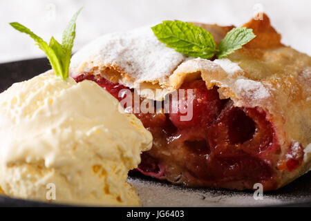 Croccante strudel di ciliegie e gelato alla vaniglia macro su una piastra orizzontale. Foto Stock