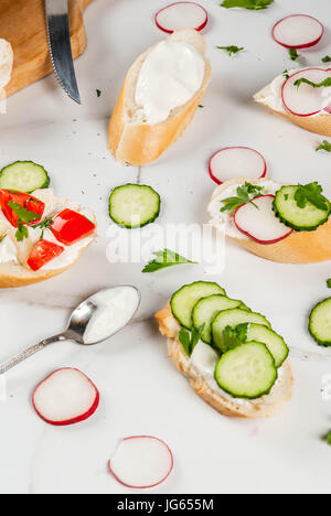 Cibo sano. Primavera, estate snack. Tostare panini fatti in casa con crema di formaggio e verdure fresche - ravanello, cetriolo, pomodoro, cipolla, peperoncino. Su Foto Stock