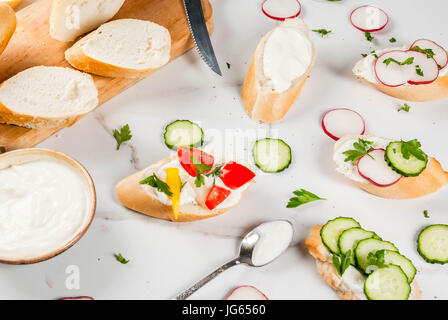 Cibo sano. Primavera, estate snack. Tostare panini fatti in casa con crema di formaggio e verdure fresche - ravanello, cetriolo, pomodoro, cipolla, peperoncino. Su Foto Stock