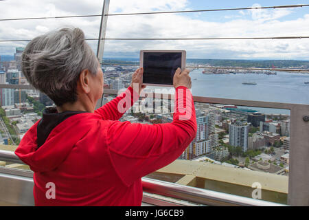 Donna con i capelli grigi è di scattare una foto con il suo tablet iPad della vista dalla Space Needle a Seattle, Washington Foto Stock