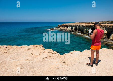 AYIA NAPA, Cipro, 15 giugno 2017: Guy battenti e facendo un'antenna video con un fantoccio DJI Pro 4 drone sopra le grotte marine di Ayia Napa, Cipro Foto Stock