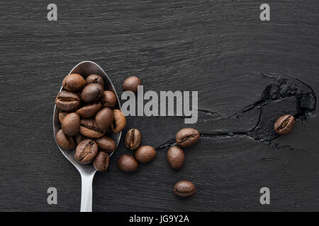 Cucchiaio di chicchi di caffè nero su sfondo di legno Foto Stock