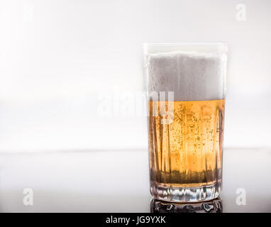 Freddo e una deliziosa birra versata in un vetro trasparente su un vetro riflettente superficie, retroilluminato Foto Stock