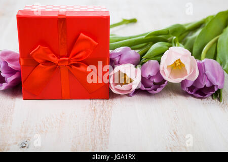 Bouquet di tulipani e un regalo su uno sfondo di legno. ancora in vita con splendidi fiori in vacanza. Foto Stock