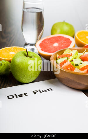 Cibo e di un foglio di carta con un programma di dieta al buio su un tavolo di legno. concetto di dieta e stile di vita sano. Foto Stock