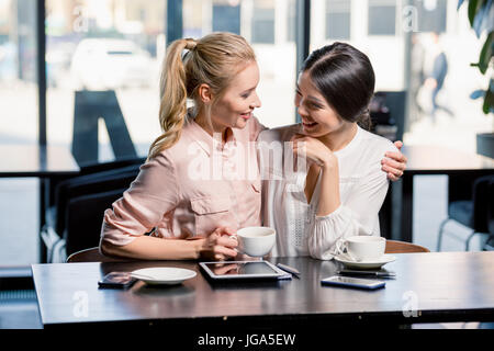 Sorridente giovani donne con tavoletta digitale mentre si beve il caffè nella caffetteria, incontro a pranzo concept Foto Stock