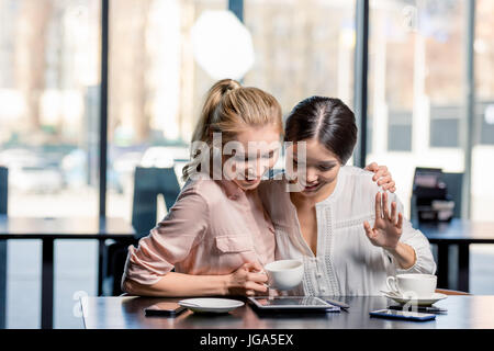 Sorridente giovani donne con tavoletta digitale mentre si beve il caffè nella caffetteria, incontro a pranzo concept Foto Stock