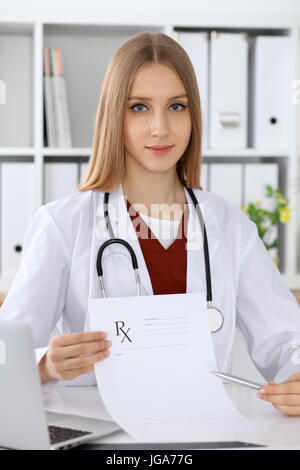 Giovani donne medico si riempie la forma medica e puntamento in prescrizione medica copia area spazio mentre guardando la telecamera Foto Stock