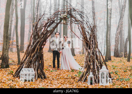 Splendida coppia di nozze sotto il misterioso hazel arch decorato con decorazioni in legno di autunno Foto Stock