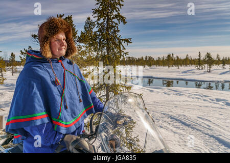 L uomo nel tradizionale abito Sami su una motoslitta, Lapponia, Svezia Foto Stock