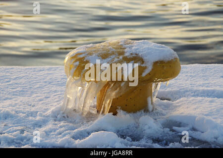 Ghiaccioli su giallo bollard ormeggio nel porto. Inverno dal mare. Foto Stock